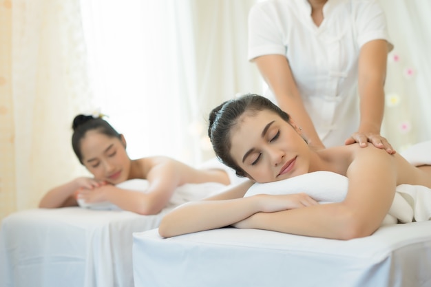 Dos mujeres jóvenes lindas disfrutan de relajarse durante el masaje en el spa.