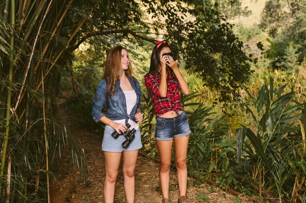 Dos mujeres jóvenes de pie en el bosque haciendo clic en fotografía con cámara