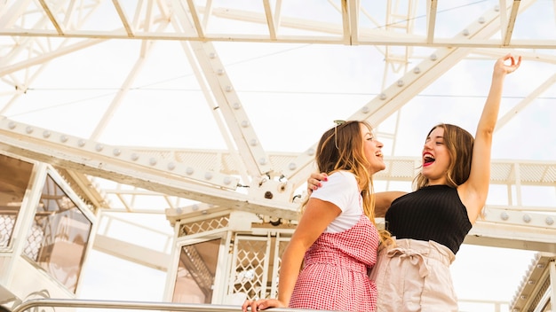 Dos mujeres jóvenes de pie delante de la noria burlándose