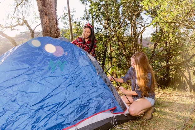 Dos mujeres jóvenes que ponen la tienda para acampar