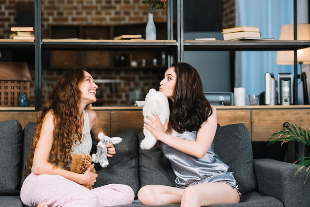 Dos mujeres jóvenes que se sientan en el sofá que sostiene el juguete suave