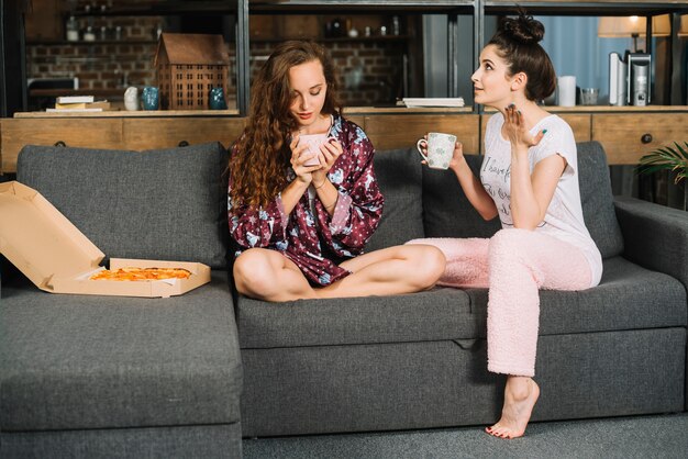 Dos mujeres jóvenes sentados en el sofá desayunando