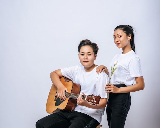 Dos mujeres jóvenes se sentaron en una silla y tocaron la guitarra.