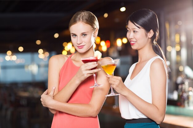 Dos mujeres jóvenes sonriendo con los cocteles en barra