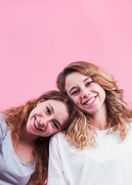 Dos mujeres jóvenes sonrientes contra fondo rosa