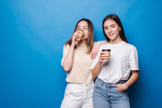 Dos mujeres jóvenes con taza de café para ir aislado en la pared azul