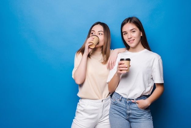 Dos mujeres jóvenes con taza de café para ir aislado en la pared azul