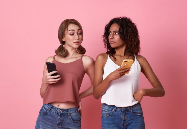 Dos mujeres jóvenes usando un teléfono móvil mientras una mujer morena mira el teléfono inteligente de su amiga