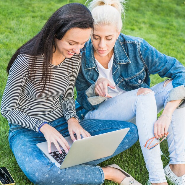 Dos, mujeres jóvenes, usar la computadora portátil, en el estacionamiento