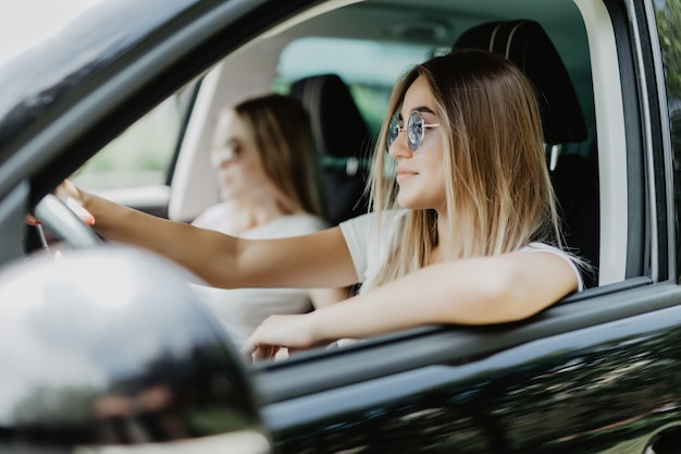 Dos mujeres jóvenes en viaje en coche conduciendo el coche y burlándose. Emociones positivas.