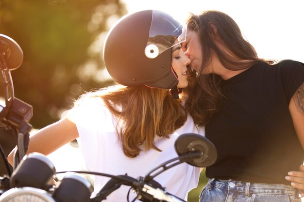 Dos mujeres lesbianas besándose en una motocicleta con cascos en