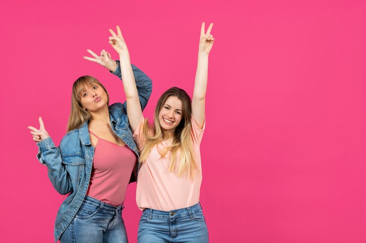 Foto gratuito dos mujeres con manos levantadas sobre fondo rosa
