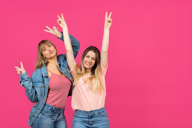 Dos mujeres con manos levantadas sobre fondo rosa