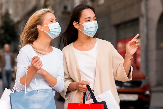 Dos mujeres con máscaras médicas y bolsas de compras para la venta de compras