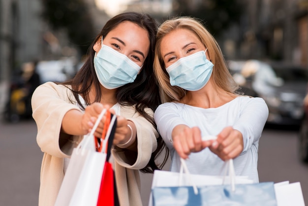 Dos mujeres con máscaras médicas posando junto con bolsas de la compra.