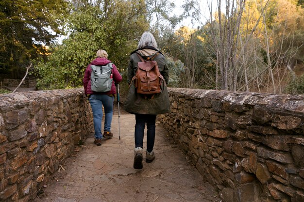 Dos mujeres mayores cruzando un puente de piedra mientras están en la naturaleza