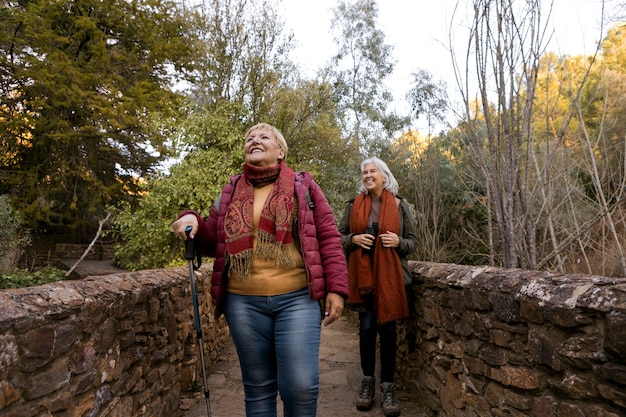 Foto gratuita dos mujeres mayores cruzando un puente de piedra mientras están en la naturaleza