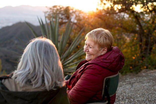 Dos mujeres mayores en una escapada a la naturaleza sentadas en sillas y disfrutando de su tiempo
