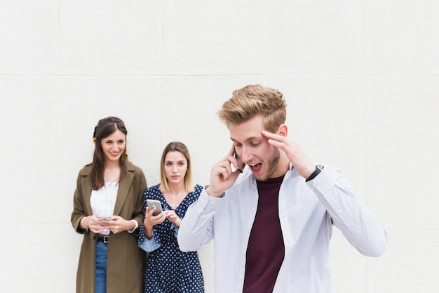 Dos mujeres mirando a hombre hablando por teléfono móvil