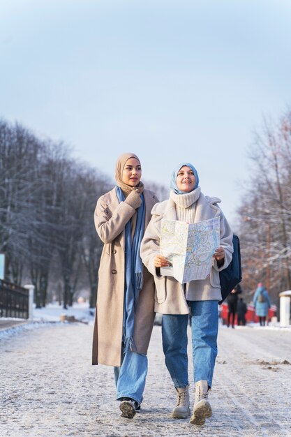 Dos mujeres musulmanas con hijabs consultando un mapa mientras viajan por la ciudad