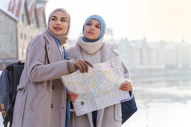 Dos mujeres musulmanas con hijabs consultando un mapa mientras viajan por la ciudad