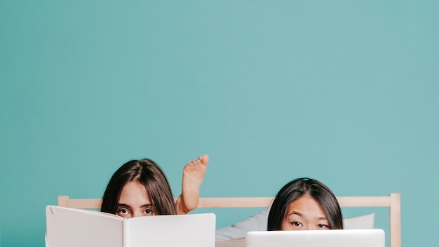 Dos mujeres que se esconden detrás del libro y la computadora portátil