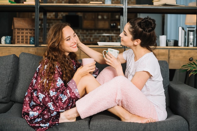 Foto gratuita dos mujeres sentadas cara a cara en el sofá sosteniendo la taza de café