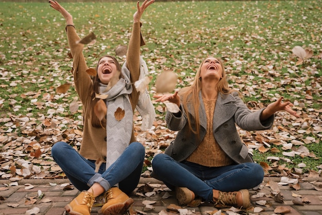 Dos mujeres sentadas y jugando con hojas en el parque