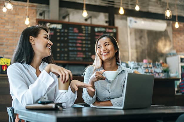 Dos mujeres sentadas y trabajando con una computadora portátil en una cafetería.