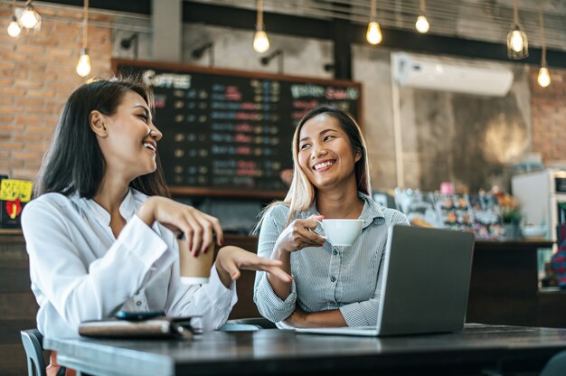 Dos mujeres sentadas y trabajando con una computadora portátil en una cafetería.