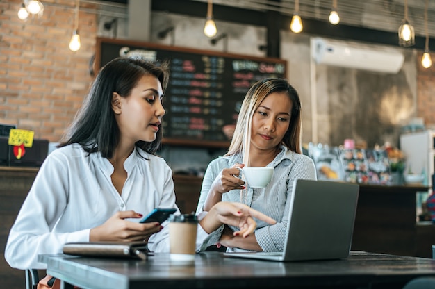 Dos mujeres sentadas y trabajando con una computadora portátil en una cafetería.