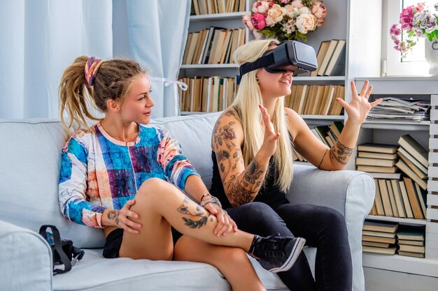 Dos mujeres sexys divirtiéndose con un dispositivo de gafas de realidad virtual en casa.