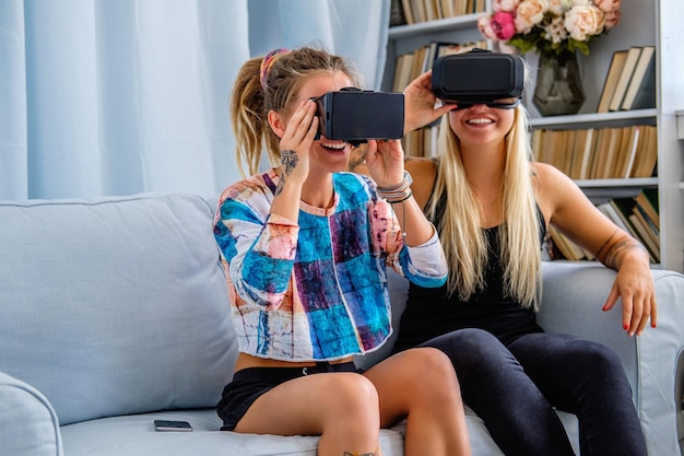 Dos mujeres sexys divirtiéndose con un dispositivo de gafas de realidad virtual en casa.