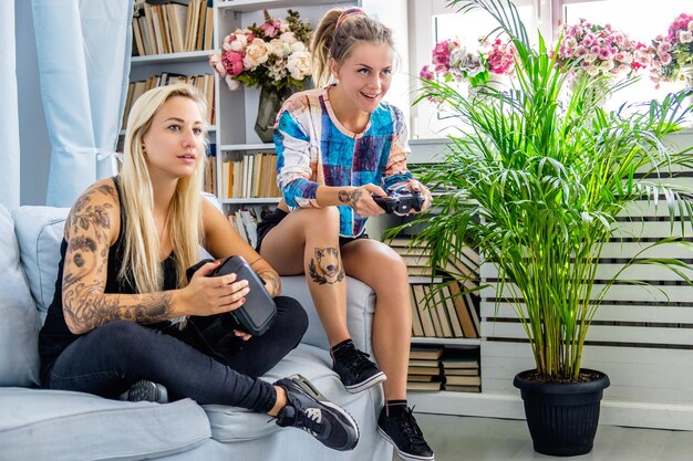 Dos mujeres sexys divirtiéndose con un dispositivo de gafas de realidad virtual en casa.