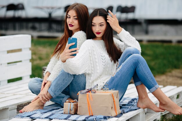 Dos mujeres se sientan en un banco afuera y disparan regalos para teléfonos inteligentes