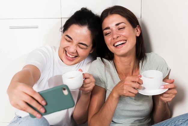 Dos mujeres sonrientes en casa en la cocina tomando un selfie