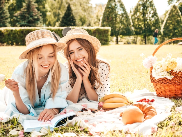 Dos mujeres sonrientes hermosas jóvenes en vestido de verano de moda y sombreros. Mujeres despreocupadas haciendo picnic al aire libre.