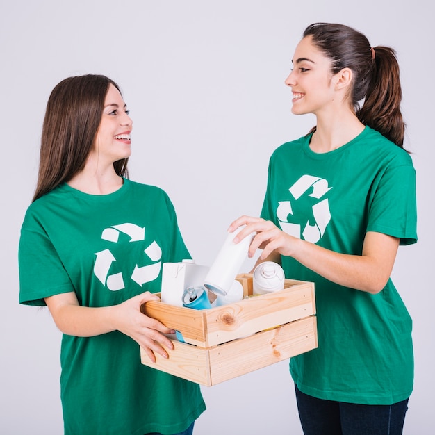 Foto gratuita dos mujeres sonrientes que sostienen la caja de madera con reciclan artículos