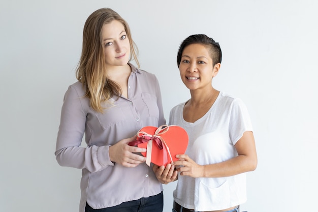 Dos mujeres sonrientes que sostienen la caja de regalo en forma de corazón roja