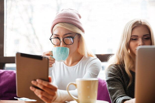 Foto gratuita dos mujeres tomando café y usando tableta en café