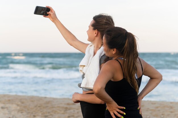Foto gratuita dos mujeres tomando selfie mientras hace ejercicio en la playa