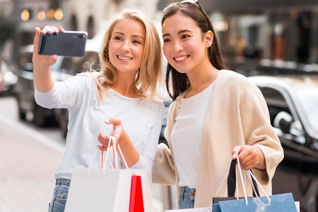 Dos mujeres tomando selfie sosteniendo muchas bolsas de la compra.