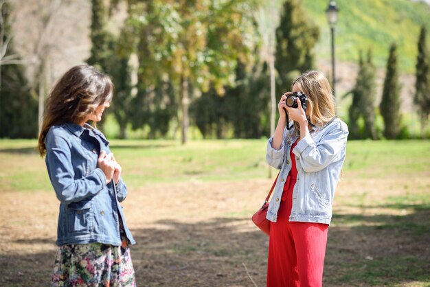 Dos mujeres turísticas jóvenes tomando fotografías con cámara réflex analógica en el parque urbano.