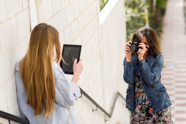 Dos mujeres turísticas jóvenes tomando fotos con tableta digital y cámara réflex analógica