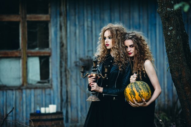 Dos mujeres vintage como brujas, posando frente a una casa abandonada en la víspera de Halloween