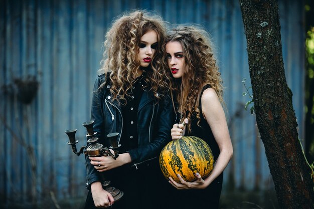 Dos mujeres vintage como brujas, posando frente a una casa abandonada en la víspera de Halloween