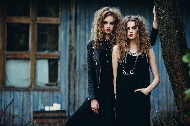 Dos mujeres vintage como brujas, posando junto a un edificio abandonado en vísperas de Halloween