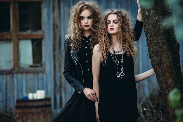 Dos mujeres vintage como brujas, posando junto a un edificio abandonado en vísperas de Halloween