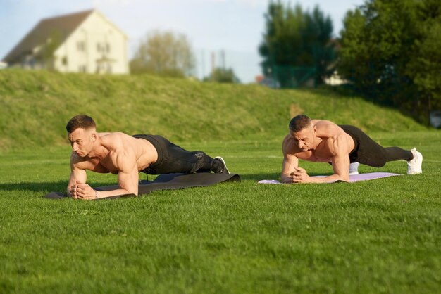 Dos musculosos culturistas haciendo ejercicios de tablones al aire libre