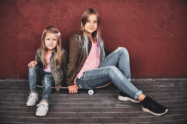 Dos niñas bonitas se relajan en la calle mientras están sentadas en la patineta.